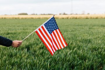 crop faceless person showing american flag on field in daytime